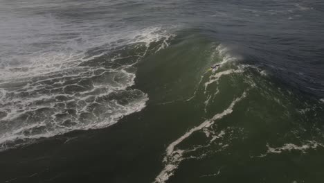 Aerial-view-of-surfer-takeoff-and-riding-a-big-wave-in-Nazaré,-Slow-motion-shot