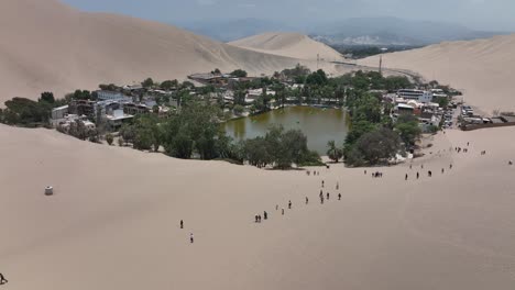 Desert-oasis-Huacachina,-Peru-with-lake-and-palms,-with-great-sand-dunes-in-the-background