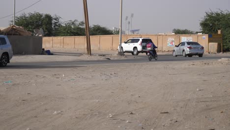 Goats-Passing-Road-Between-Cars-and-Motorbike,-Suburbs-of-Nouakchott,-Mauritania