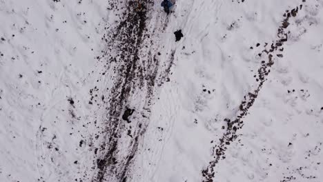 Top-down-aerial-view-of-hikers-climbing-steep-white-snowy-mountain,-forward