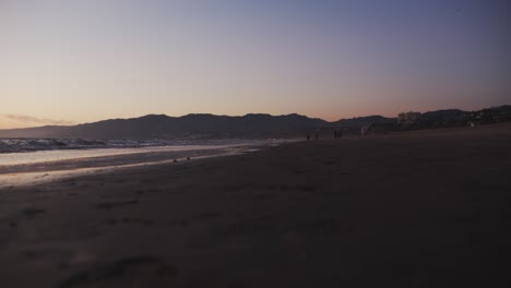 waves-on-beach-with-people-walking-in-the-distance-in-the-evening-with-mountains-in-the-background