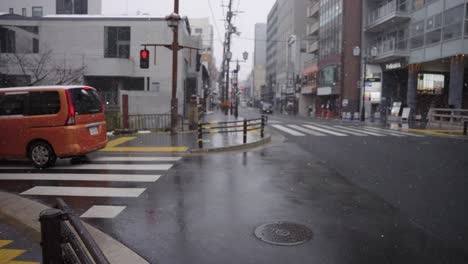 Snow-Falls-in-Sanjo-District-of-Kyoto,-Cars-Driving-Through-Wet-Town