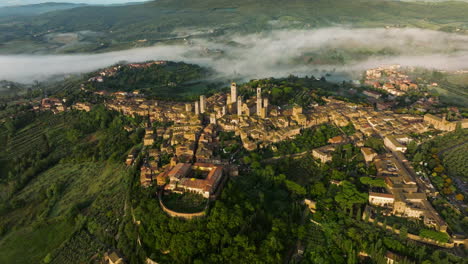 Volar-Sobre-La-Ciudad-De-Mediana-Edad-De-San-Gimignano-Rodeada-De-Verdes-Colinas-En-Un-Brumoso-Amanecer-En-Toscana,-Italia