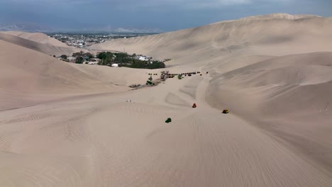 Oasis-Del-Desierto-Huacachina,-Perú-Con-Lago-Y-Palmeras,-Con-Grandes-Dunas-De-Arena-En-El-Fondo