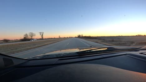 Point-of-view-through-the-front-window-while-driving-on-a-interstate-with-little-traffic-past-farmland-and-fields