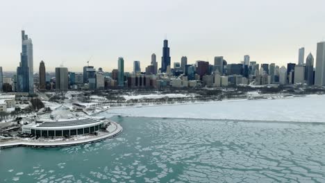 Aerial-view-over-icy-Lake-Michigan-towards-the-Grant-park-and-the-Chicago-skyline,-during-a-cloudy-winter-day