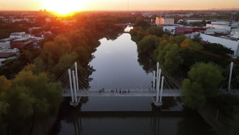Bird's-eye-perspective-on-sunset-over-a-river-with-cityscape-panorama-and-pedestrian-bridge