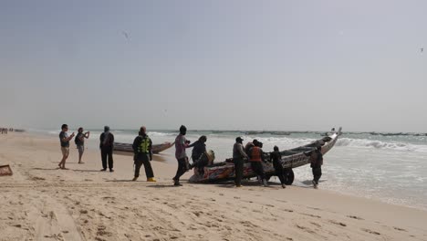 Gente-Africana-Empujando-Un-Barco-De-Pesca-En-La-Playa-Frente-A-Las-Olas-Del-Océano-Atlántico