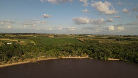 Aerial-wide-shot-of-coast-of-Fray-Bentos-and-farm-fields-in-background-during-sunset-time-in-Uruguay