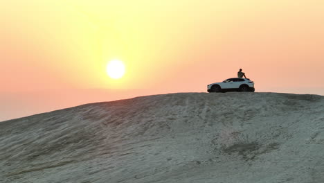 Man-sits-on-a-desert-hill-overlooking-a-sunrise-in-ontop-of-a-Mazda-car