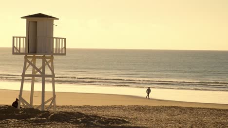 Lifeguard-hut-on-the-shore-of-a-beach,-and-person-running-in-slow-motion-at-sunset