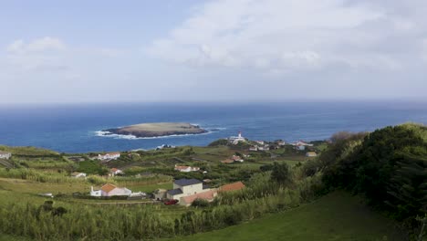 rural-coastal-village-with-a-lighthouse-and-an-island-in-the-Atlantic-ocean,-cloudy-sky-in-Topo,-São-Jorge-island,-the-Azores,-Portugal