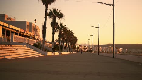 A-peaceful-seaside-walk-at-sunset,-with-ocean-views-and-palm-trees-lit-by-street-lamps