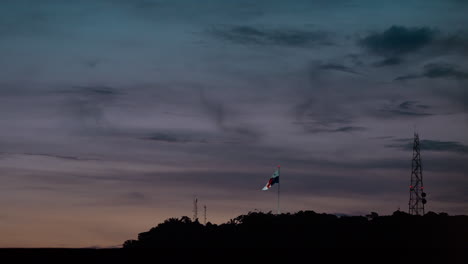 Broadcast-tower-and-streaming-Panama-flag-at-sunset-on-Cerro-Ancon,-Panama-City