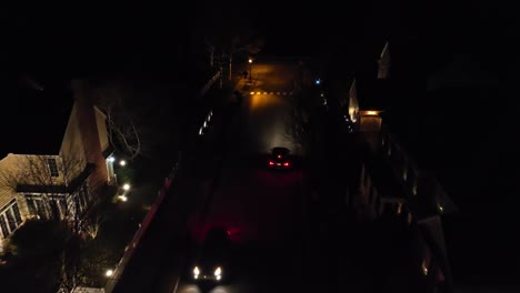 Aerial-tracking-shot-of-two-cars-passing-each-other-in-dark-neighborhood-at-night