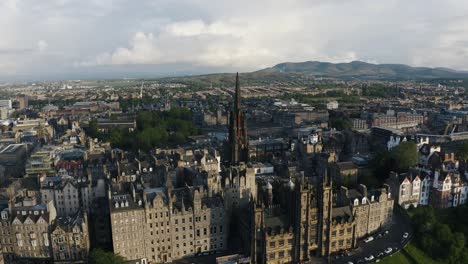 Aerial-view-of-downtown-Edinburgh-buildings-surrounded-by-lush-countryside,-featuring-a-tall-chapel-in-the-center