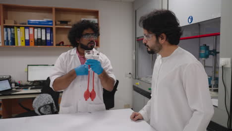 Indian-scientist-explaining-scientific-device-working-with-Arabic-team-member-in-research-laboratory,-slow-pull-back
