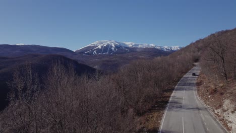 Cars-passing-by-a-mountain-road-with-a-snowy-mountain-in-the-background