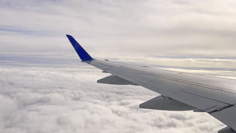 Close-up-of-airplane-wing-surface-flying-high-over-clouds