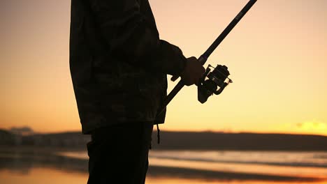Man-silhouette-handle-rotation-with-reel-of-fishing-rod-against-of-orange-sunset-slow-motion