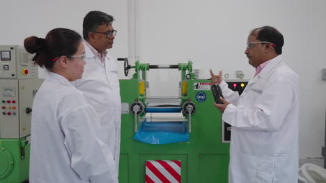 Indian-scientist-explaining-manufacturing-process-to-team-in-front-of-industrial-laboratory-machinery