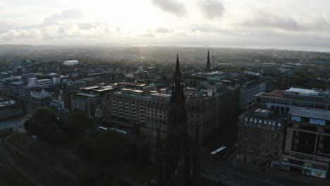 Aerial-shot-of-the-tall-Scott-Monument-and-all-of-downtown-Edinburgh,-Scotland-during-a-bright-sunrise