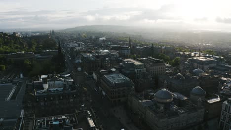 Drone-shot-of-downtown-Edinburgh,-Scotland-near-sunset-with-a-clock-tower-overlooking-the-neighborhood