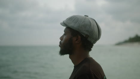 Close-up-of-a-handsome-young-black-bearded-man-in-a-beret-looking-out-over-the-ocean-introspectively