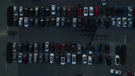 Top-down-aerial-shot-of-dark-parking-lot-full-of-cars-and-busy-with-cars-entering-and-exiting-parking-spots