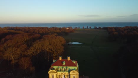 Reveal-iconic-hunting-lodge-on-sunny-evening-in-Danish-landscape,-aerial-view