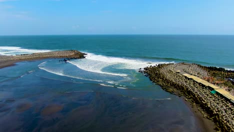 Black-sand-Glagah-Beach-lagoon,-ocean-waves-crush-on-breakwater,-Java,-Indonesia