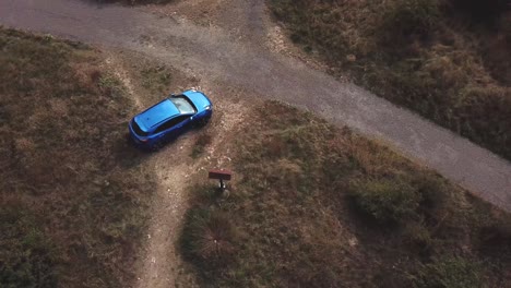 Aerial-top-view-over-a-blue-Ford-Puma-parked-next-to-a-country-crossroads