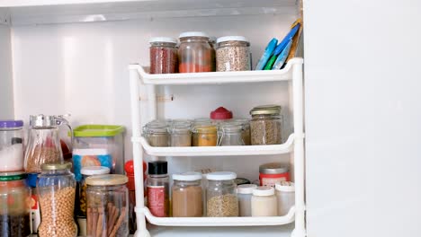 Jars-of-spices-and-ingredients-in-kitchen-cupboard,-truck-shot