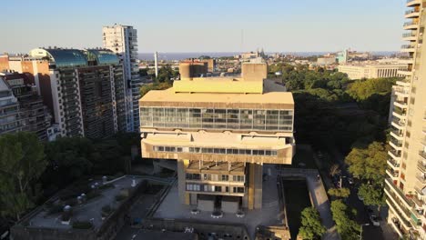 Aerial-rising-over-brutalist-style-National-Library-between-buildings-and-trees-at-golden-hour,-Buenos-Aires