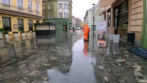 Street-Sweeper-Walking-a-Rainy-Pedestrian-Street-in-Central-Celje,-Slovenia