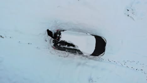 Man-removing-heavy-snow-cape-from-cars-roof-in-winter-season,-aerial-view-top-down
