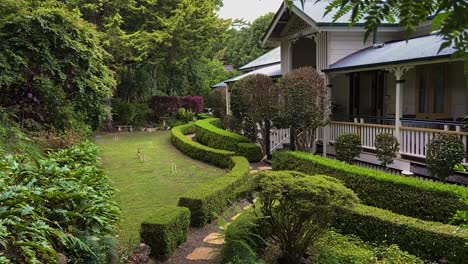 Smooth-cinematic-descending-reveal-shot,through-lush-foliage,-of-a-classic-traditional-country-Queenslander-house,-nestling-in-neatly-manicured-landscaped-garden