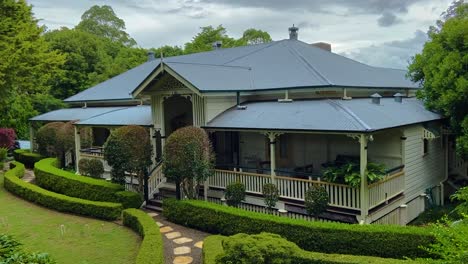 Smooth-slow-cinematic-panning-shot-of-a-classic-traditional-country-Queenslander-house,-nestling-in-neatly-manicured-landscaped-garden-deep-in-the-Queensland-Hinterland