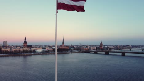 Lettische-Fahnenwelle-Mit-Der-Majestätischen-Stadt-Riga-Im-Hintergrund,-Luftbild
