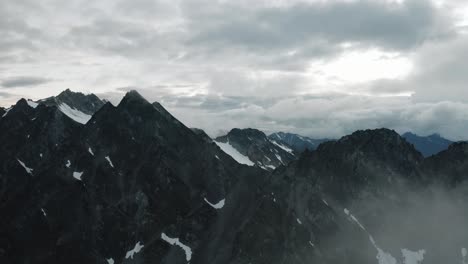 Alaskan-Rugged-Mountain-Range,-Drone-Flying-through-the-Clouds-and-Mountains-at-Sunset