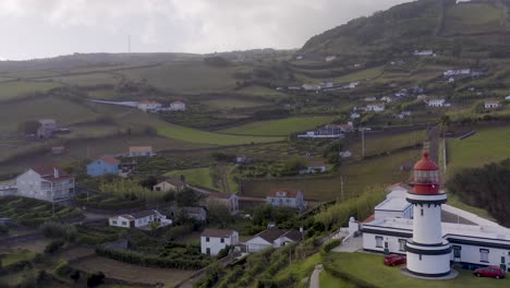 Drone-view-of-a-village-with-a-lighthouse,-cloudy-sky-in-Topo,-São-Jorge-island,-the-Azores,-Portugal