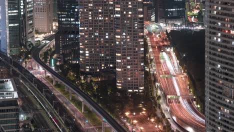 Tráfico-Y-Tren-Que-Viaja-En-La-Ciudad-De-Tokio-Por-La-Noche-Pasando-Por-Condominios-Y-Hoteles-Desde-El-Observatorio-Superior-Junto-Al-Mar-Del-Centro-De-Comercio-Mundial-En-Tokio,-Japón