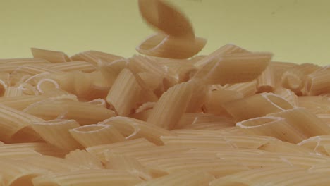 Makro-Von-Fallenden-Trockenen,-Halb-Gefurchten-Stiften-Oder-Mezze-Penne-Rigate-Pasta-Auf-Gelbem-Hintergrund