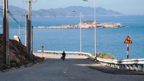 Cafe-racer-motorbike-driving-up-seaside-road-in-Vietnam,-going-surfing-with-the-board-and-kite