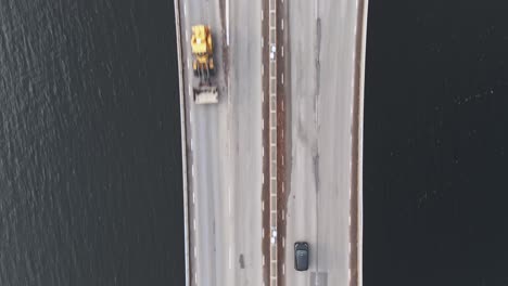Vehicle-driving-through-highway-bridge-over-water-in-aerial-top-down-view