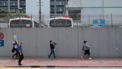 Fußgänger-Gehen-An-Einer-Polizeistation-Vorbei,-Die-In-Hongkong-Durch-Eine-Große,-Hohe-Graue-Mauer-Und-Einen-Stachelzaun-Geschützt-Ist