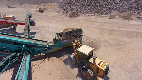 Cinematic-drone-shot-of-an-excavator-loading-rocks-on-a-conveyer-belt-in-a-rock-quarry