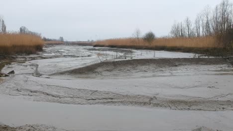 Push-in-rising-aerial-dried-up-river-bed-rainy-day-mud-puddle-landscape