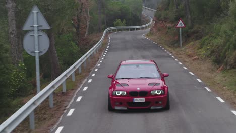Ominous-luxury-red-BMW-car-driving-towards-camera-on-rural-winding-Barcelona-country-road