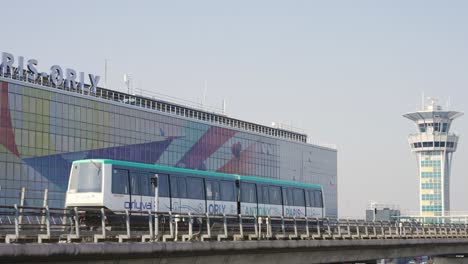 Orlyval-Moderner-U-bahn-shuttle,-Der-Am-Flughafen-Paris-Orly-Und-Dem-Kontrollturm-Vorbeifährt